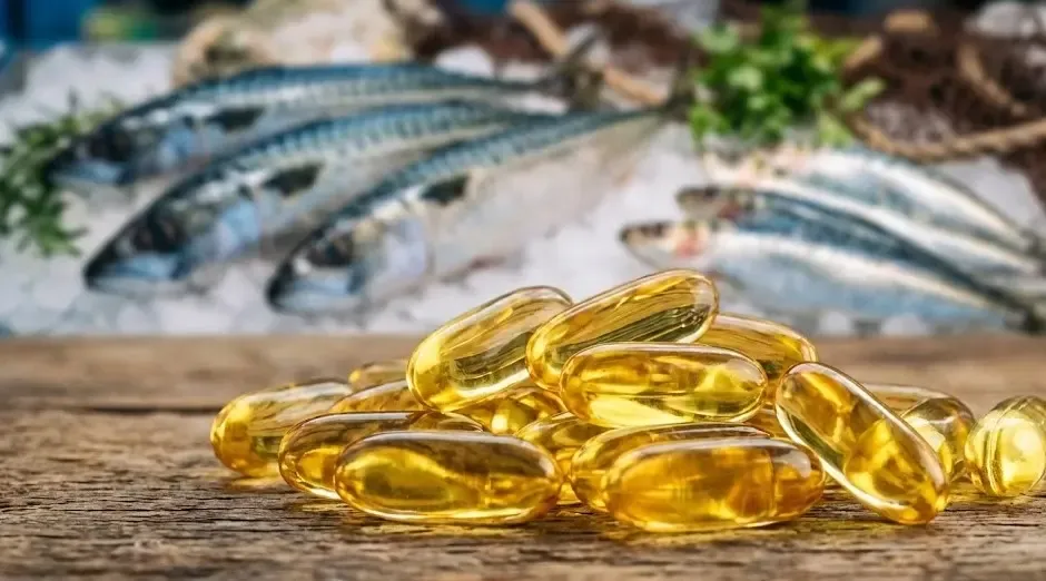 Cápsulas doradas de Omega-3 en primer plano con un fondo desenfocado de pescado azul fresco