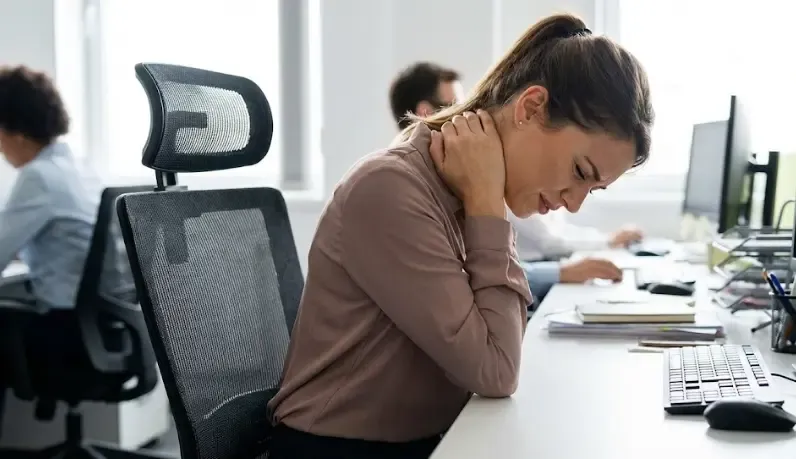 Persona en la oficina tocándose el cuello con expresión de dolor por mala postura